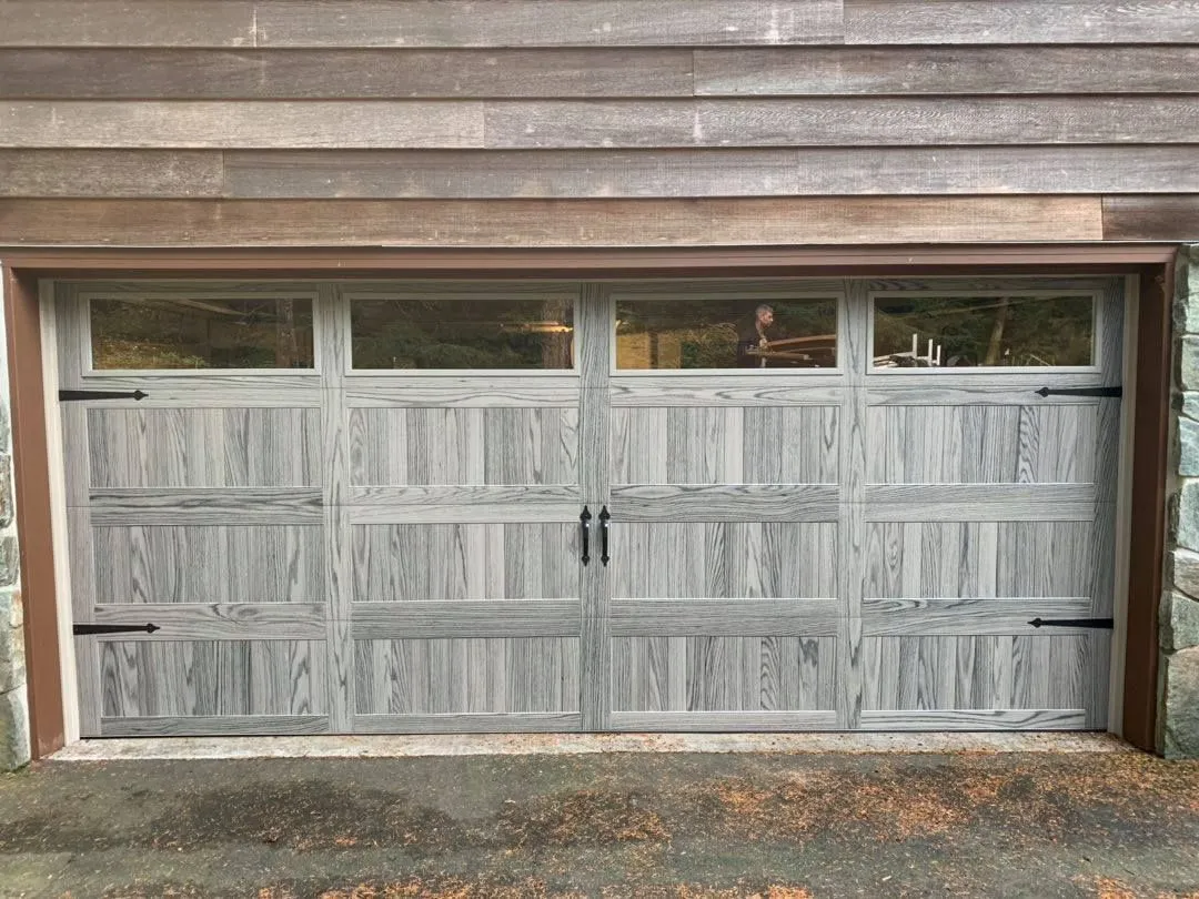 Grey woodgrain carriage-house garage door with black strap hinges and a row of windows