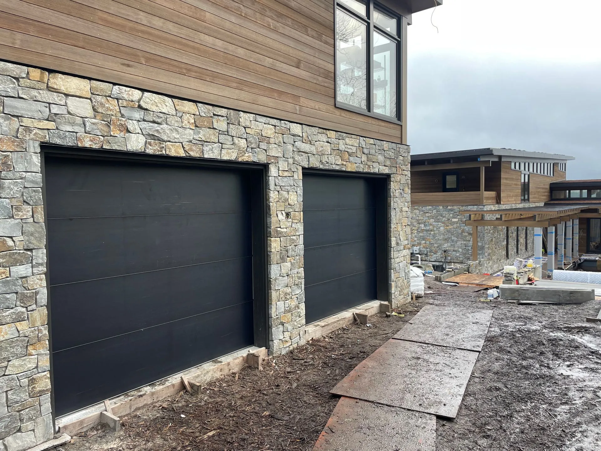 9x8 Northwest Door Modern Tech garage doors in dark bronze set in a stone and cedar facade
