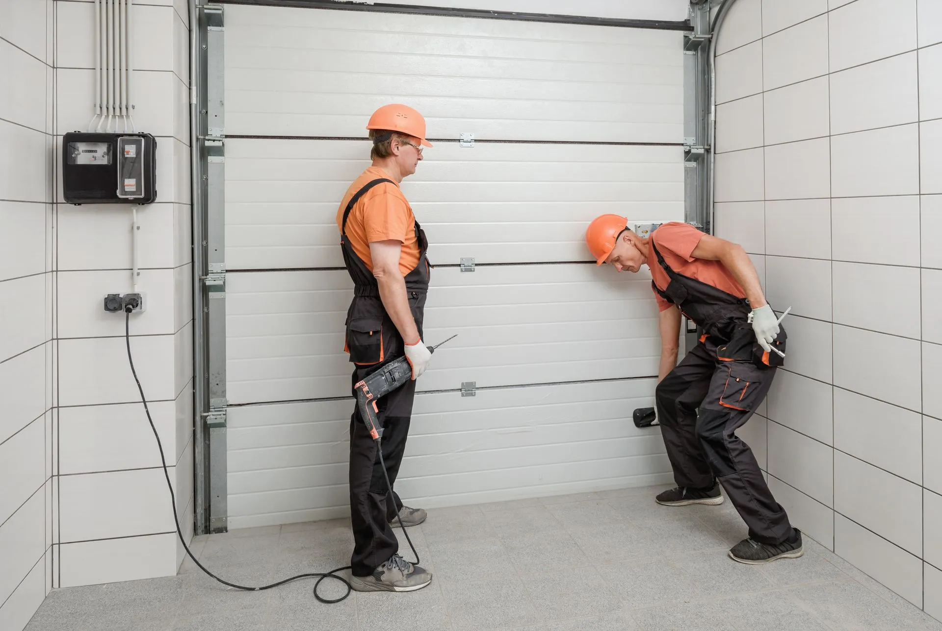 Two technicians in hard hats fitting a white sectional garage door